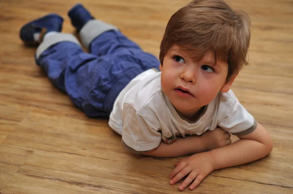 Curious small boy lying on wooden floor — Stock Photo, Image