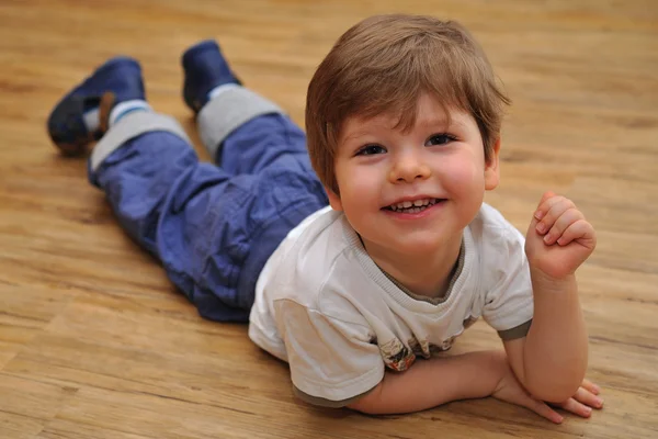 Felice piccolo ragazzo sdraiato sul pavimento in legno — Foto Stock