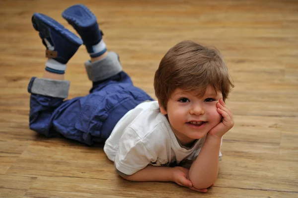 Felice relax piccolo ragazzo sdraiato sul pavimento in legno — Foto Stock
