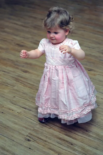 Nyfiken liten flicka som går i rosa klänning på trägolv — Stockfoto