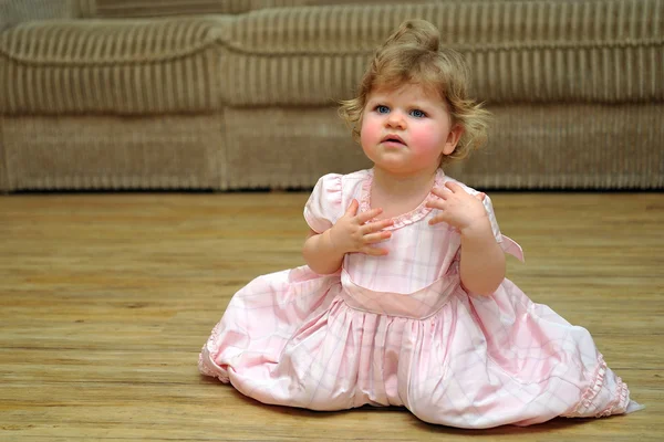 Astonished small girl in pink dress on wooden floor — Stock Photo, Image