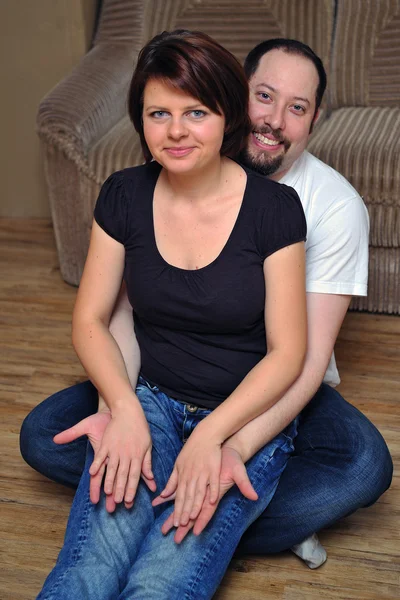 Happy couple sitting on wooden floor — Stock Photo, Image