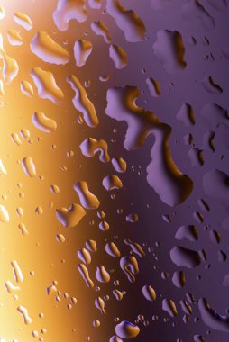 Cam yüzeyindeki su damlacıklarının çok renkli arkaplanı yansıtan soyut görüntüsü.