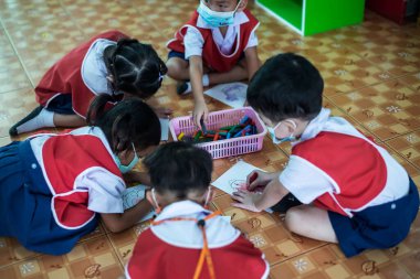 CHIANG MAI, THAILAND - 23 Mart 2021: Taylandlı çocuklar anaokulunda kağıt üzerinde mum boyamakla eğleniyorlar. Chiang Mai, Tayland 'da