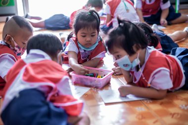 CHIANG MAI, THAILAND - 23 Mart 2021: Taylandlı çocuklar anaokulunda kağıt üzerinde mum boyamakla eğleniyorlar. Chiang Mai, Tayland 'da