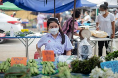 CHIANG MAI, THAILAND - 5 Temmuz 2021: Bir kız öğrenci günlerini Tayland, Chiang Mai 'de açık hava pazarında sebze satarak geçiriyor.