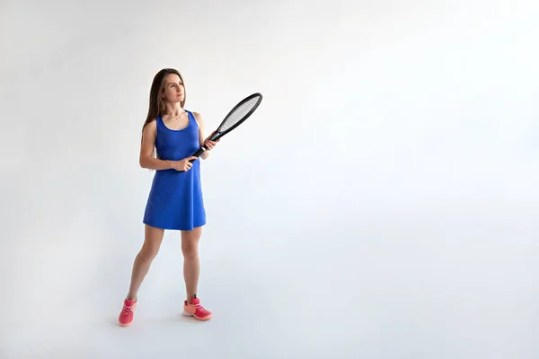 Une jeune femme en forme avec une raquette à la main dans une robe bleue pour le jeu grand tennis sur un fond blanc. — Photo