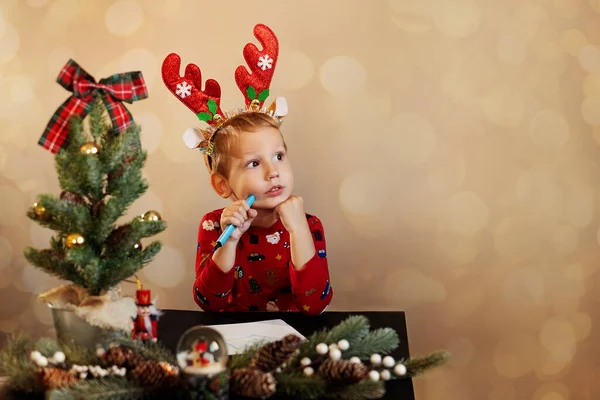 Çocuk Noel ağacının yanında Noel Baba 'ya mektup yazıyor..