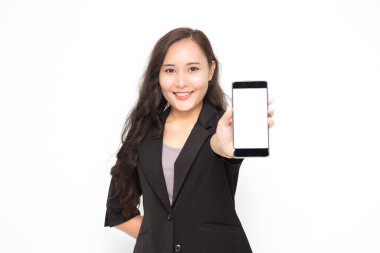 Siyah takım elbiseli güzel Asyalı iş kadını elinde akıllı bir telefonla beyaz arka plan ve fotokopi alanında bir şeyler sunuyor. Kendine güvenen Asyalı çalışan kadın gülümsüyor ve neşeli.