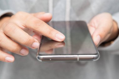 Gri gömlekli bir kadının elinde akıllı telefon tutarken yakın plan fotoğrafı. Kadın sosyal medya konsepti hakkında konuşuyor.