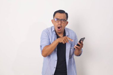 Kızgın Asyalı adam cep telefonunu işaret ederken ayakta duruyor. Beyaz arkaplanda izole