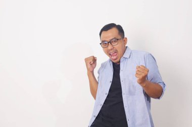 Mutlu, enerjik, Asyalı genç bir adam beyaz stüdyo arka planında izole edilmiş bağırıp yumruklarını sıkıyor.