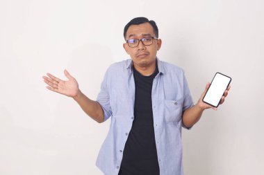 Teknoloji, online yaşam tarzı konsepti. Sinirli ve hoşnutsuz genç Asyalı adamın portresi. Cep telefonunu korku ve şaşkın bir ifadeyle gösteriyor. Beyaz arkaplanda izole