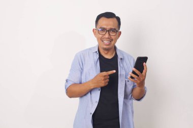 Cep telefonunu işaret ederken ayakta duran mutlu Asyalı adam. Beyaz arkaplanda izole