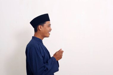 Asyalı Müslüman adam elinde bir şey tutarken ayakta duruyor. Beyazda izole edilmiş