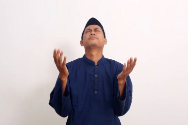 Müslüman dinine mensup genç bir Asyalı beyaz arka planda yalnız dua ediyor.