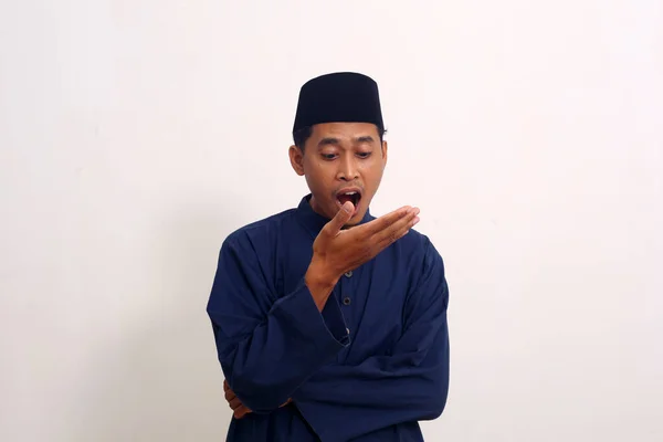 Bad breath. Halitosis concept. Portrait of asian muslim man checking his breath with his hand