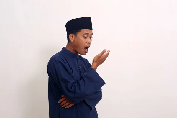 Bad breath. Halitosis concept. Portrait of asian muslim man checking his breath with his hand