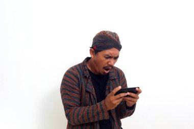 Java kostümlü kızgın Asyalı adam akıllı telefonuyla oyun oynarken ayakta duruyor..