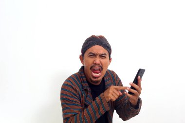 Çekici Asyalı genç adam telefonunu işaret ediyor, kötü haberler alıyor, şok edici kızgın bir jest yapıyor.