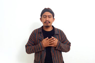 Geleneksel Java kostümlü Asyalı adam göğsünü tutarken ayakta duruyor. Rahatlamış hissediyor.