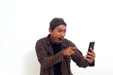 Geleneksel Java kostümlü Asyalı adam hücresinden iyi haberler okurken ayakta duruyor.