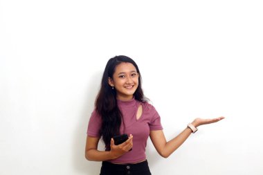 Güzel Asyalı genç bir kız elinde cep telefonu tutarken bir şey sunuyor. Beyaz arka planda izole edilmiş.