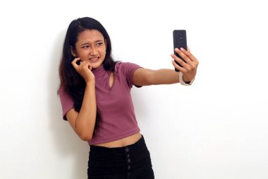 Korkak Asyalı genç kız cep telefonundan haber alırken ayakta duruyor. Beyazda izole edilmiş