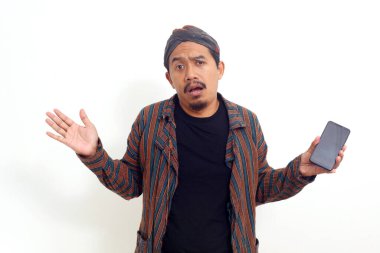 Kafası karışmış Asyalı bir adam cep telefonu tutarken ayakta duruyor. Beyaz arkaplanda izole