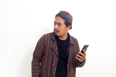 Kızgın Asyalı adam yan bakarken ve cep telefonu tutarken ayakta duruyor. Beyaz arkaplanda izole