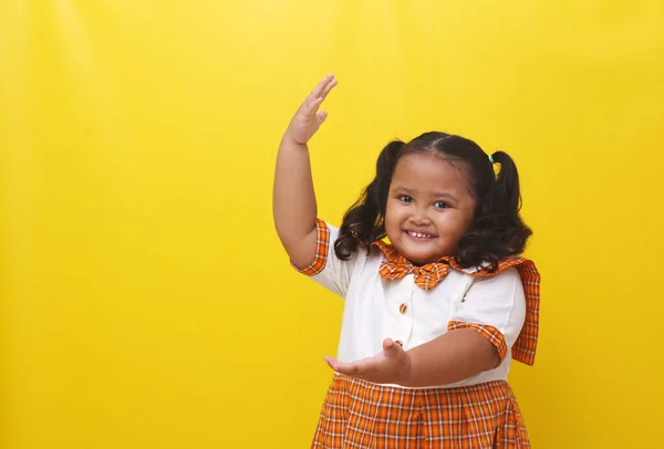 Aziatisch Schoolmeisje Staat Terwijl Iets Presenteert Geïsoleerd Gele Achtergrond — Stockfoto