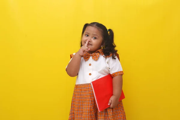 Asian Little Schoolgirl Standing While Holding Book Silence Finger Gesture —  Fotos de Stock