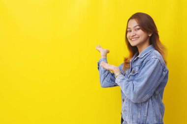 Dost canlısı Asyalı genç bayan yan bir şeyler gösteriyor. Kopyalama alanı ile sarı arkaplanda izole
