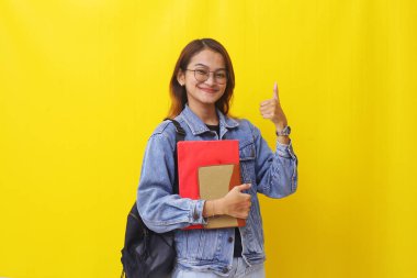 Neşeli Asyalı genç bir kadın kitap tutarken ve baş parmağını kaldırırken. İzole edilmiş