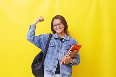 Başarılı bir Asyalı genç kadın elini sıkarken ve kitapları tutarken ayakta duruyor. Sarıda izole edilmiş.