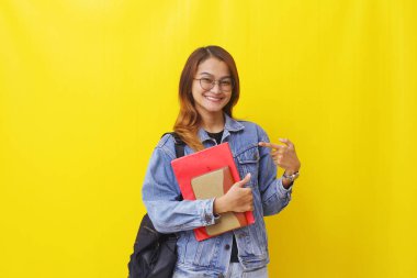 Asya 'nın genç ve güzel üniversitesi bir şeyi işaret ederken ayakta duruyor. Sarı arkaplanda izole edilmiş