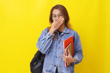 Genç Asyalı üniversite öğrencisi kitap tutarken ve ağzını kapatırken ya da jest yaparken.