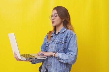 Dizüstü bilgisayar tutarken Asyalı genç bir öğrencinin ayakta durmasına şaşırdım. Sarı arkaplanda izole edilmiş