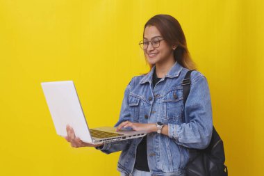 Elinde dizüstü bilgisayarla gülümseyen Asyalı üniversite öğrencisi. Sarı arkaplanda izole edilmiş