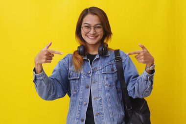 Bir şey sunarken ayakta duran mutlu Asyalı üniversite öğrencisi. Sarı arkaplanda izole edilmiş