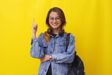 Çekici genç Asyalı üniversite öğrencisi boş alanı işaret ederken ayakta duruyor. Sarıda izole edilmiş.