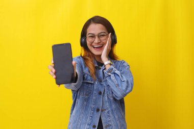 Asyalı genç bir kadının kulaklık kullanırken boş bir cep telefonu ekranı göstermesinin mutlu ifadesi.