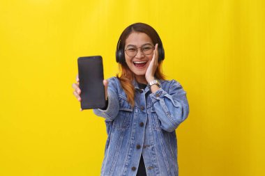 Enerjik genç Asyalı kadın kulaklık kullanırken boş bir cep telefonu ekranı gösteriyor.