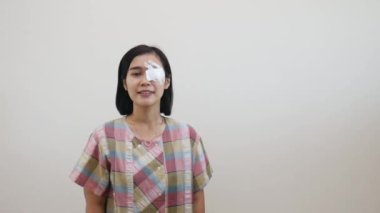 Göz koruyucusuyla duran Asyalı kadın boş alanı işaret ediyor. Eğitim tedavisi, göz ameliyatı sonrası ya da katarakt cerrahi konsepti. Beyaz duvarda izole edilmiş..