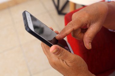 Close up photo of elderly woman's and operating cellular phone. Hand touching mobile phone screen