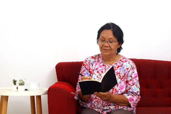 Пожилая Азиатка Сидящая Диване Пишущая Книге Изолированный Белом Фоне — стоковое фото