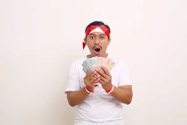 Wow expression of asian man while standing and holding indonesian banknotes.Independence day concept