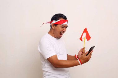 Heyecanlı Endonezyalı adam cep telefonundan iyi haberler alırken ayakta duruyor. Bağımsızlık Günü konsepti.