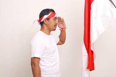 Asian man standing while respecting indonesian flag. Independence day concept. Isolated on white