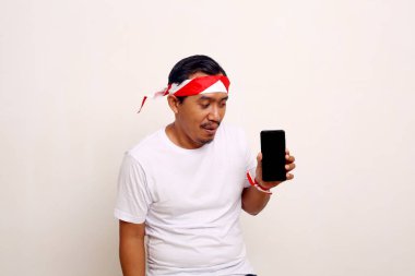 Asian man standing while presenting blank cell phone screen with indonesian independence day concept